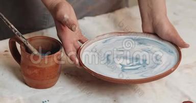 熟练的陶工釉从红泥中覆盖盘子。 关上门。 进程。 陶瓷车间。